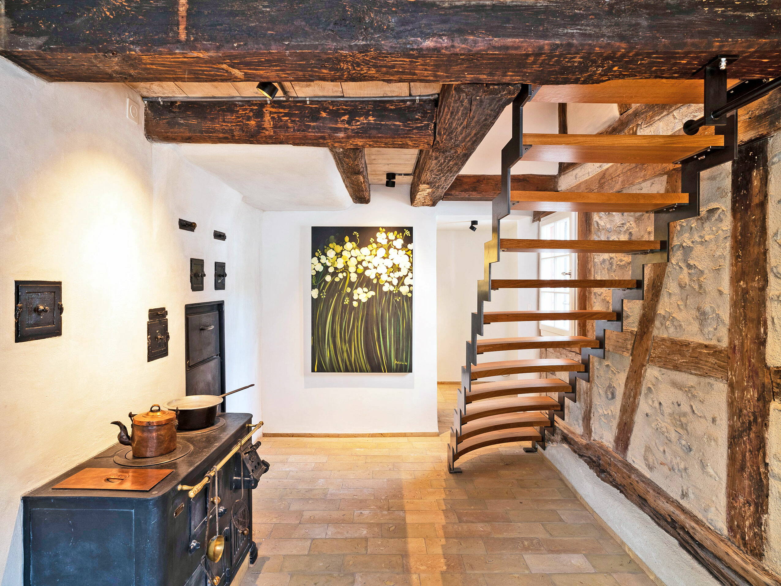 Zoom: Sicht in einen Raum mit alten Holzbalken an der Decke und einer Treppe aus Holz und Metall in den zweiten Stock.