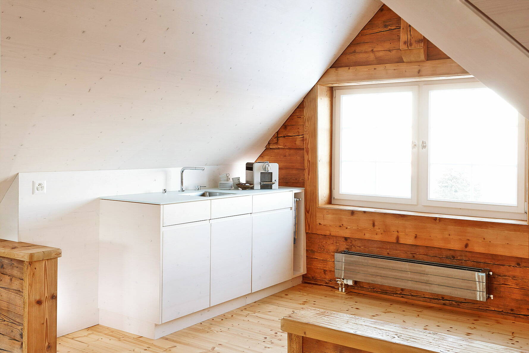 Zoom: Schlichte, moderne Küche in Holz gearbeitet im Dachstock eines Altbaus mit grosszügigem Fenster.