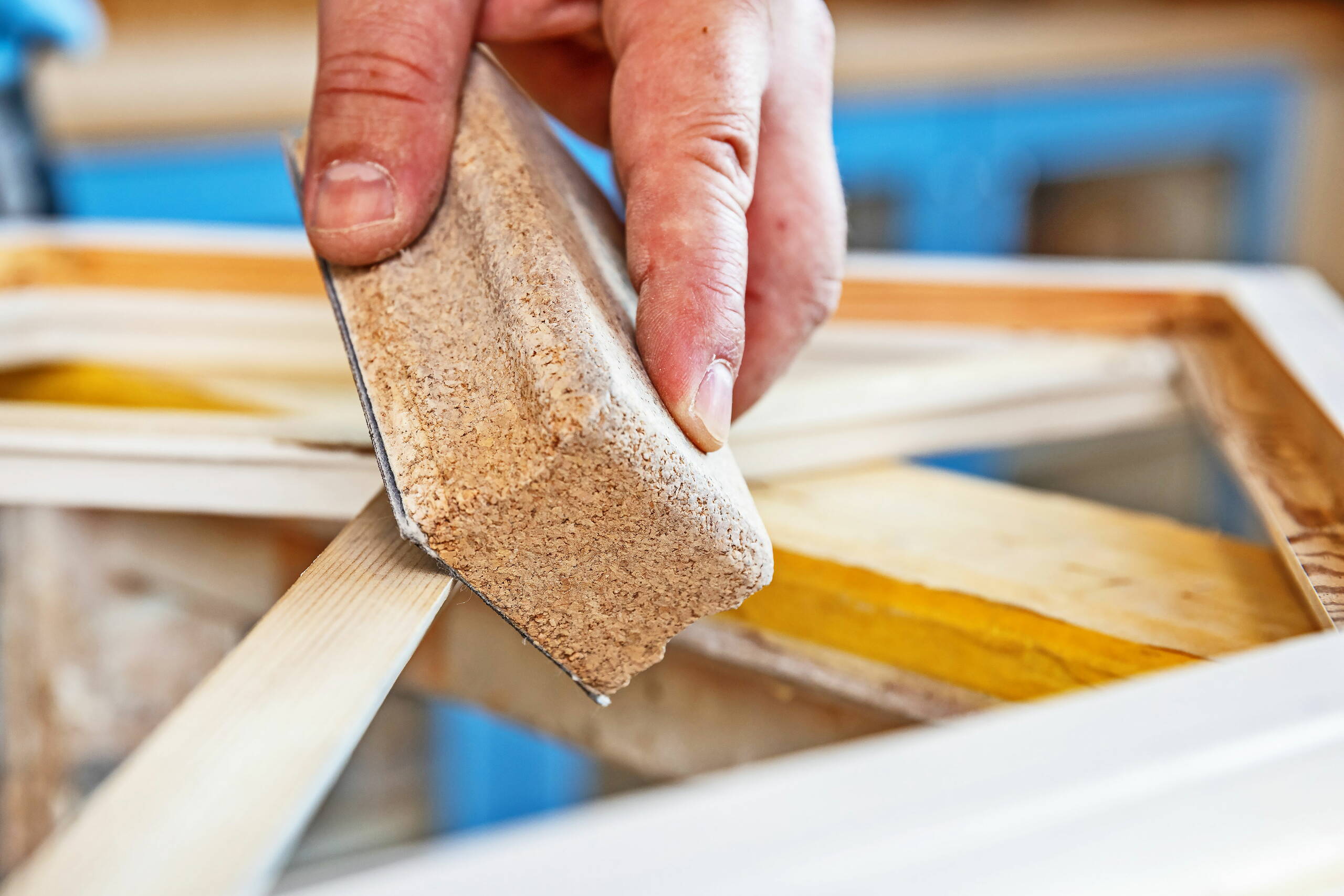 Ein Fensterbauer schleift mit einem Schleifblock die Holzelemente eines Fensterrahmens.