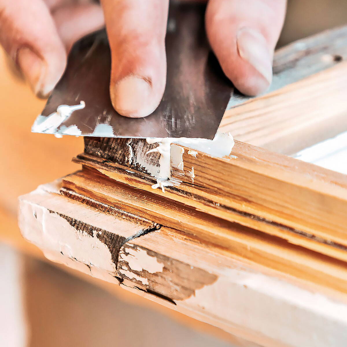 Fensterbauer spachtelt mit einem Werkzeug die Fugen eines Fensterrahmens aus Holz.