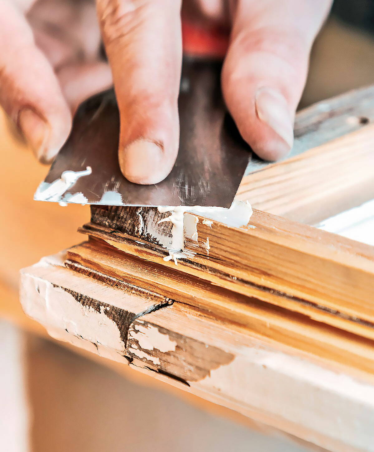 Fensterbauer spachtelt mit einem Werkzeug die Fugen eines Fensterrahmens aus Holz.