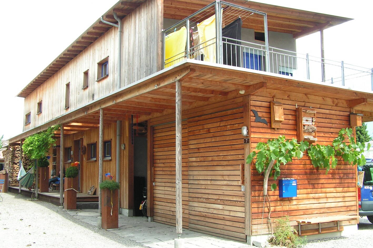 graue verputzte fassade eines mehrfamilienhauses mit grossen fenstern mit spiegelung von himmel, wolken und bäumen