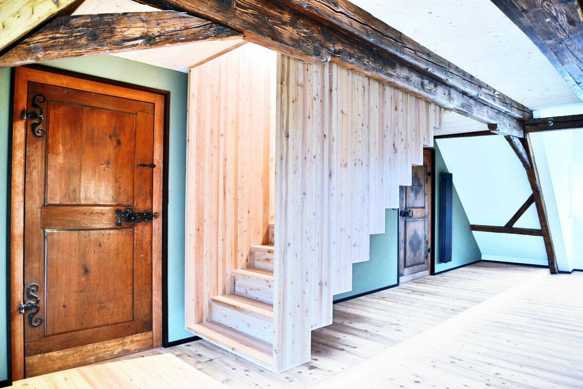 Sicht auf eine an der Decke befestigten, über dem Boden schwebenden Treppe aus Holz in einem Altbaugebäude.